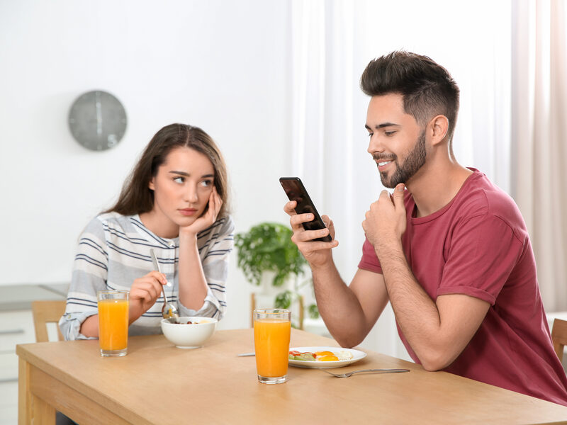 Partner absorbed in a phone at breakfast while the other waits — ADHD couples therapy Los Angeles